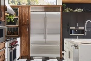 Refrigerador de la Serie Sub-Zero Classic integrado en gabinetes personalizados de madera teñida en una cocina iluminada por el sol y terrosa